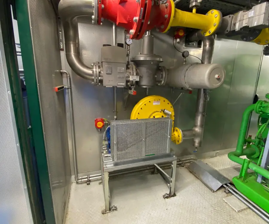 Industrielle Rohrleitungen mit roten und gelben Ventilen, verbunden mit einem großen runden Manometer.
