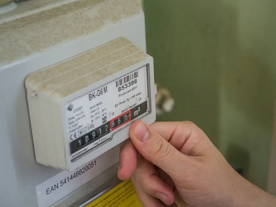 Hand hält ein Blatt Papier vor einem Gaszähler, der 10912,865 m³ anzeigt.